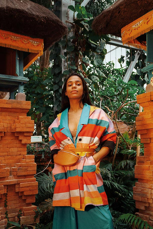 Model among Balinese temples in the gardens of the world, wearing colorful striped jacket combined with brown fanny pack